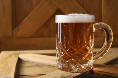 Mug with fresh beer on wooden crate, closeup. Space for text