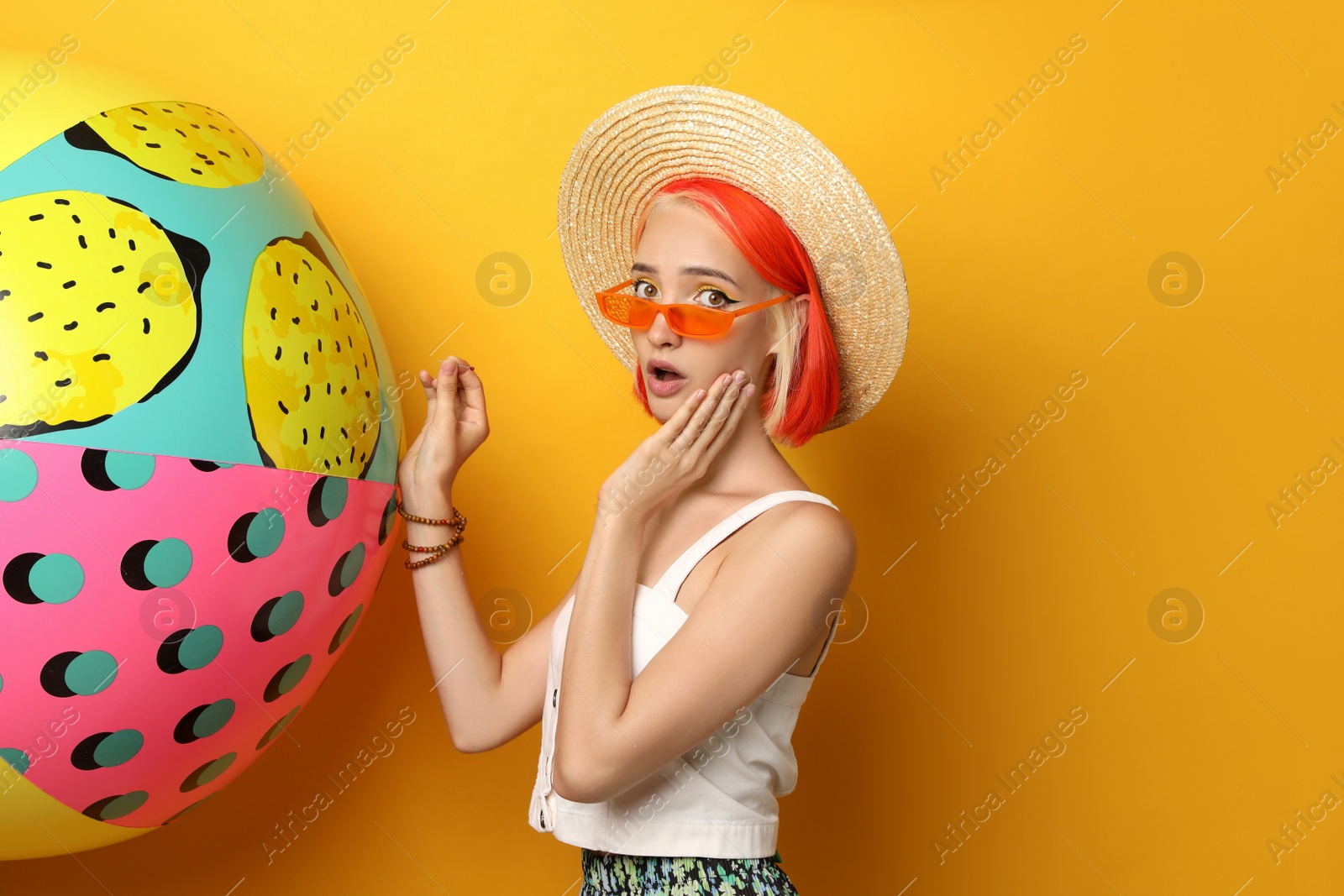 Photo of Emotional young woman with bright dyed hair and inflatable ball on orange background