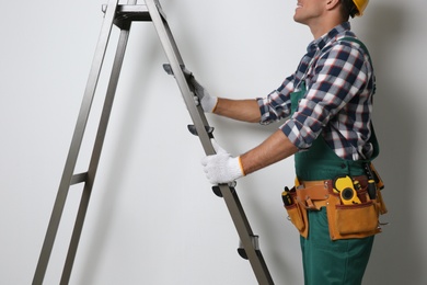 Photo of Professional builder with metal ladder on light background, closeup