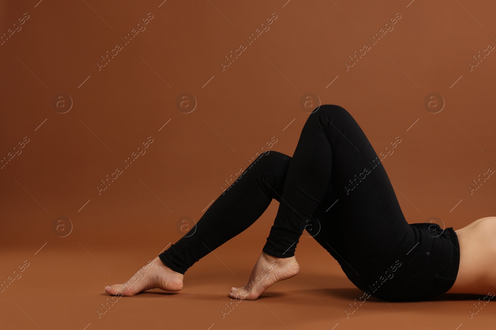 Photo of Woman wearing stylish black jeans on brown background, closeup. Space for text