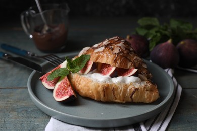 Photo of Delicious croissant with figs and cream served on light blue wooden table