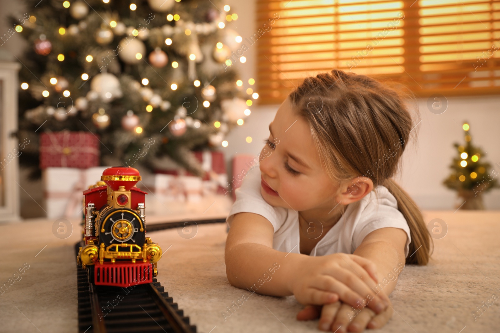 Photo of Little girl playing with colorful train toy in room decorated for Christmas