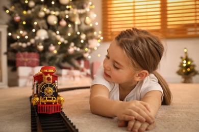 Little girl playing with colorful train toy in room decorated for Christmas