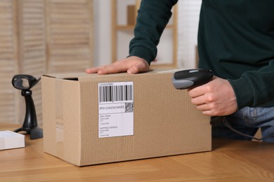 Photo of Seller with scanner reading parcel barcode at table in office, closeup. Online store