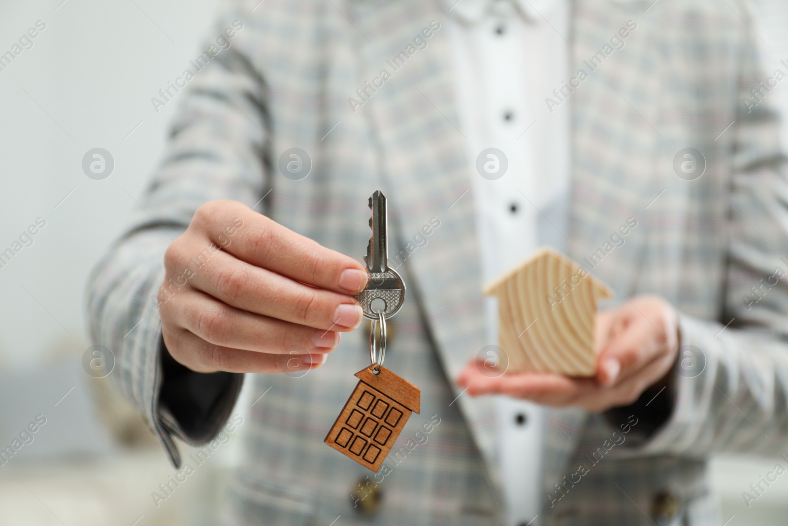 Photo of Real estate agent holding house figure and key indoors, closeup