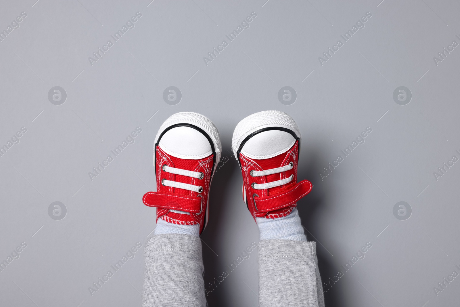 Photo of Little child in stylish red gumshoes on light grey background, top view