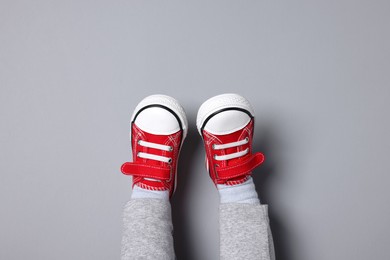 Photo of Little child in stylish red gumshoes on light grey background, top view