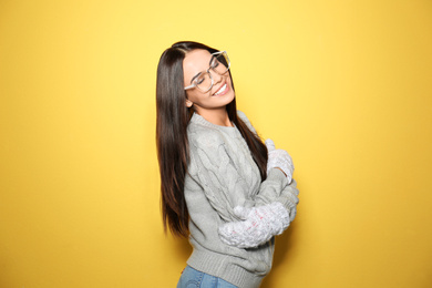 Happy young woman wearing warm sweater and mittens on yellow background 