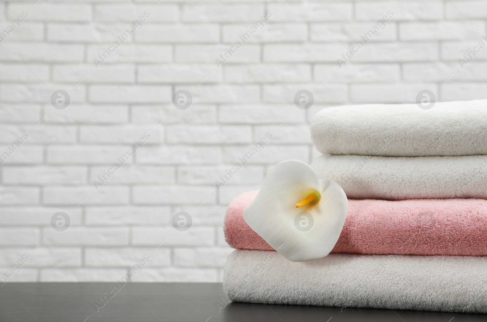 Photo of Stack of folded soft towels with flower on table near brick wall. Space for text