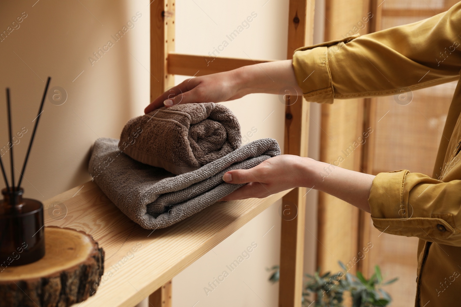 Photo of Woman putting towels onto shelf indoors, closeup