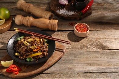 Photo of Stir-fry. Tasty noodles with meat and vegetables served on wooden table, space for text