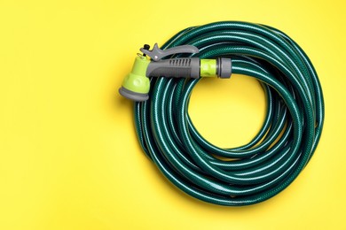 Watering hose with sprinkler on yellow background, top view. Space for text