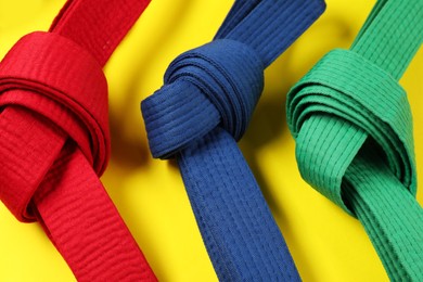 Photo of Colorful karate belts on yellow background, closeup