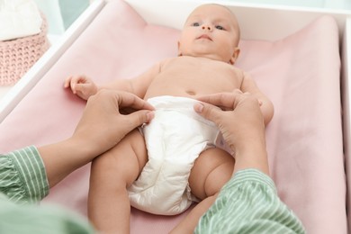 Mother changing her baby's diaper on table at home