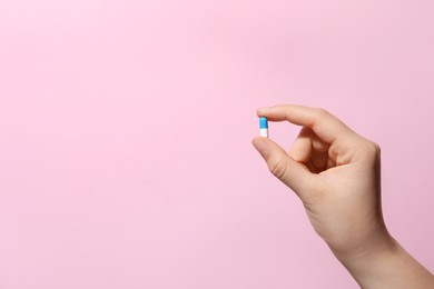 Photo of Woman holding pill on pink background, closeup. Space for text