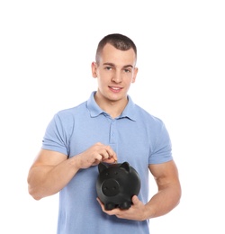 Photo of Young man putting coin into piggy bank on white background