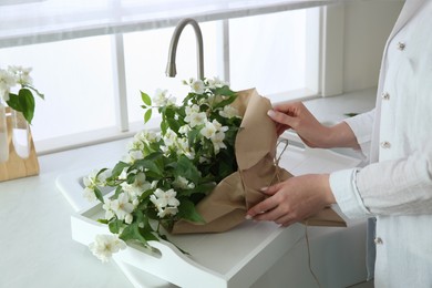 Photo of Woman making bouquet with beautiful jasmine flowers in kitchen, closeup