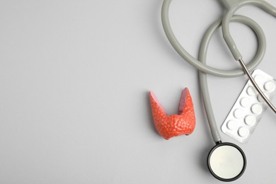 Photo of Plastic model of healthy thyroid, pills and stethoscope on grey background, flat lay. Space for text