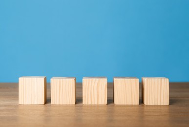 Photo of Empty cubes in row on wooden table against light blue background. Space for text