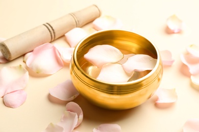 Photo of Golden singing bowl with petals and mallet on beige background. Sound healing