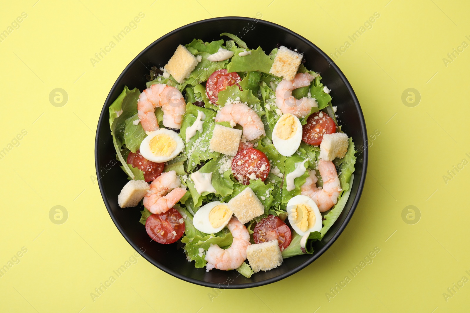 Photo of Delicious Caesar salad with shrimps on yellow background, top view