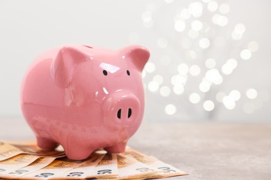 Photo of Piggy bank with euro banknotes on grey table against blurred lights, space for text