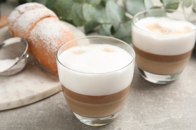 Delicious latte macchiato and croissant on light grey table