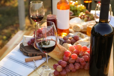 Photo of Red wine and snacks served for picnic on wooden table outdoors