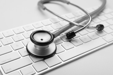 Keyboard and stethoscope on beige background, closeup