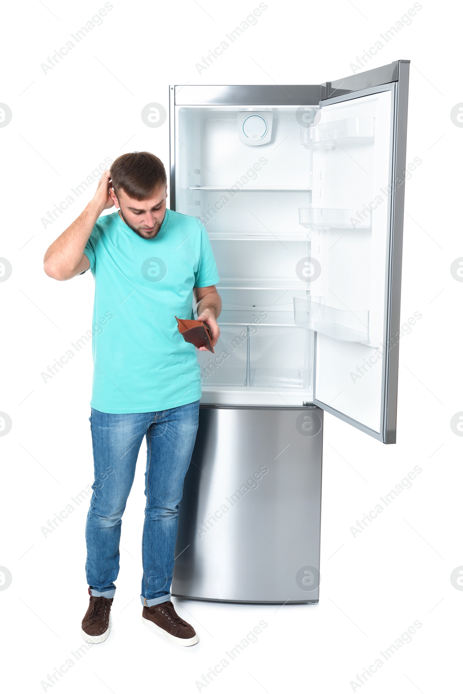 Photo of Young man with no money in wallet near empty refrigerator on white background