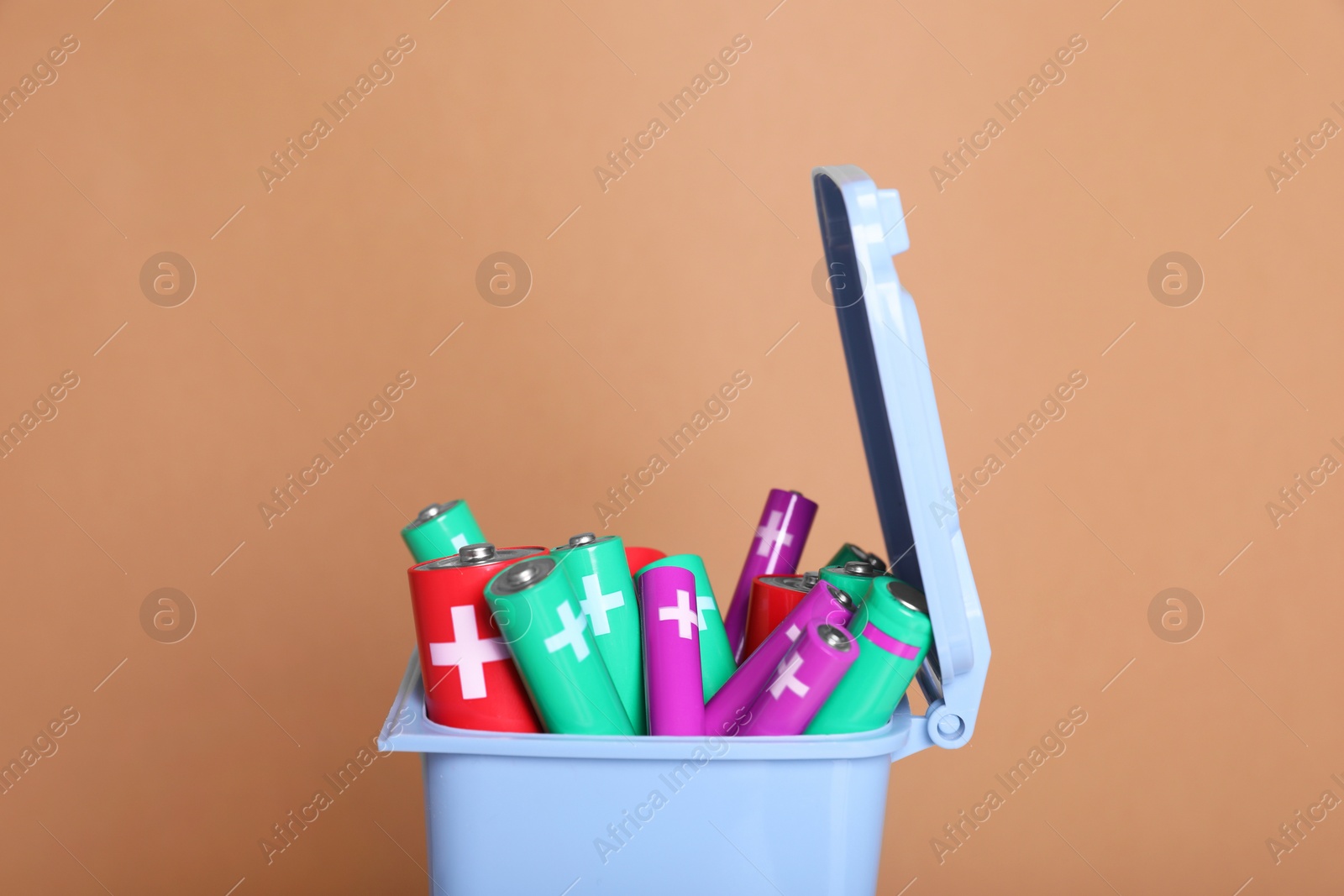 Photo of Many used batteries in recycling bin on light brown background