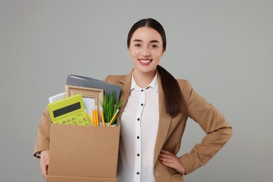 Happy unemployed woman holding box with personal office belongings on grey background