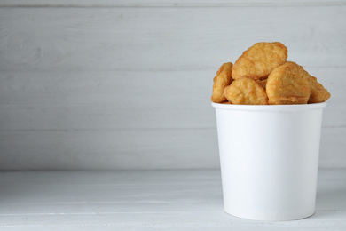 Photo of Bucket with tasty chicken nuggets on white wooden table. Space for text