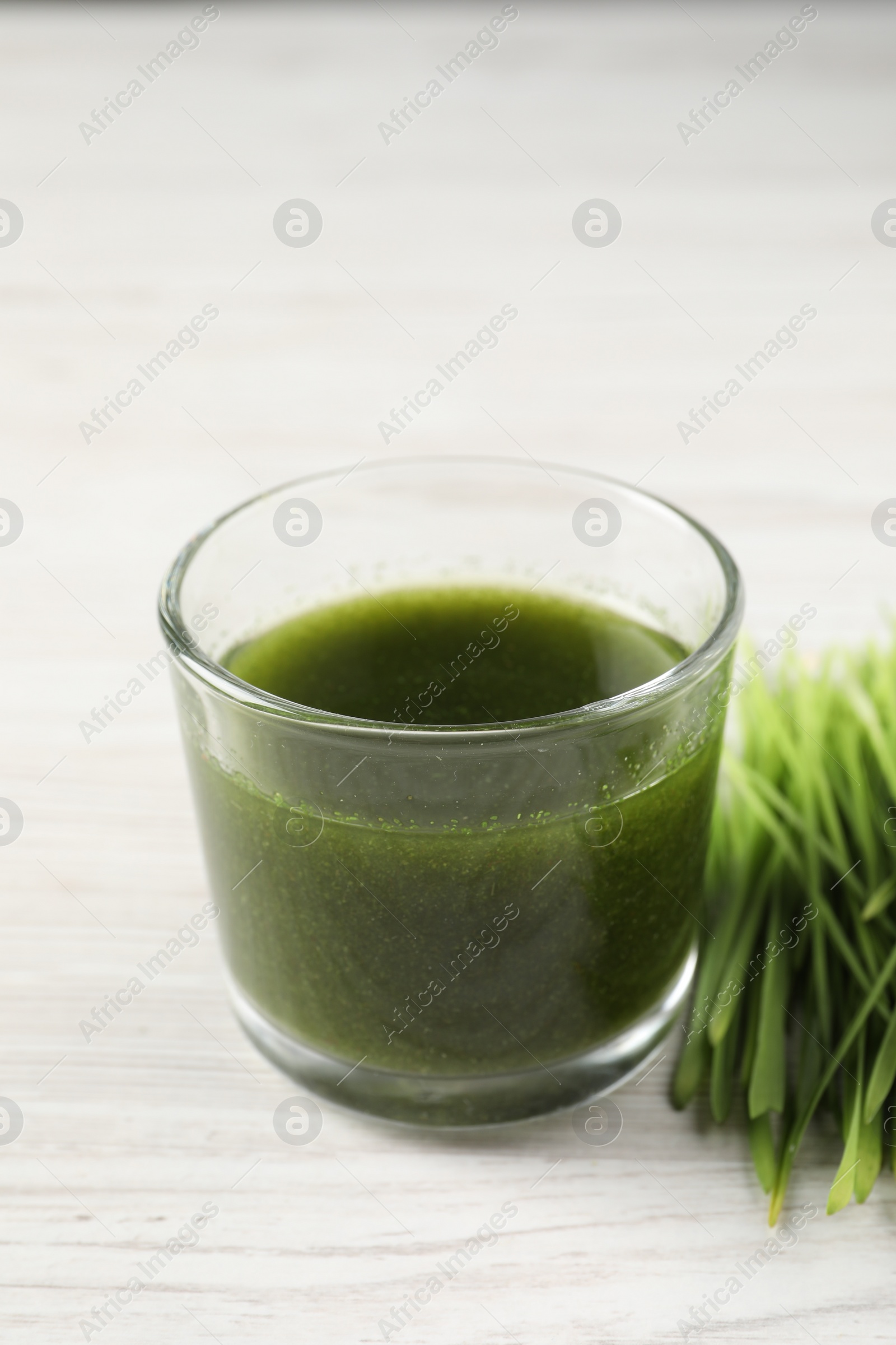 Photo of Wheat grass drink in glass and fresh sprouts on white wooden table, closeup