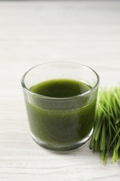 Photo of Wheat grass drink in glass and fresh sprouts on white wooden table, closeup