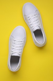 Pair of stylish white sneakers on yellow background, top view