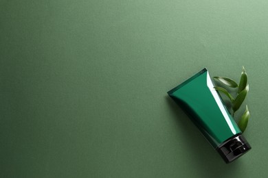 Tube of men's facial cream and leaves on green background, flat lay. Space for text