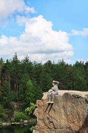 Young man on rock near lake and forest. Camping season