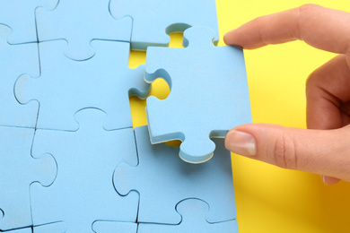 Woman putting light blue puzzle piece on yellow background, closeup. Career promotion concept