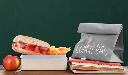 Image of Lunch box with appetizing food and bag on wooden table near green chalkboard