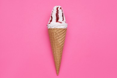 Photo of Delicious ice cream with raspberry jam in waffle cone on pink background, top view