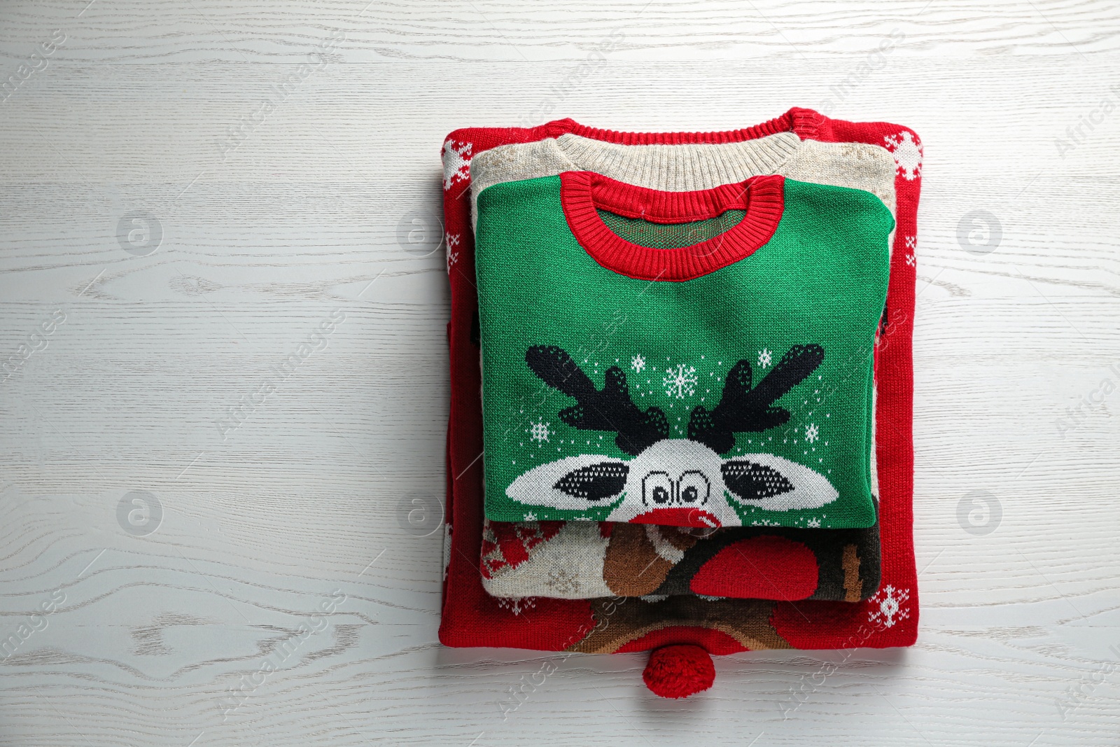 Photo of Folded warm Christmas sweaters on white wooden table, top view. Space for text