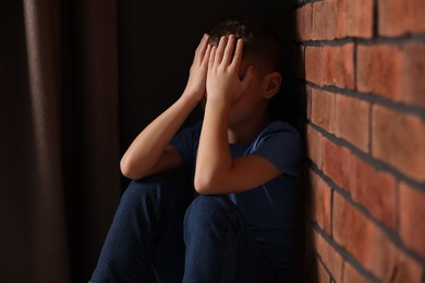 Photo of Child abuse. Upset boy near brick wall indoors