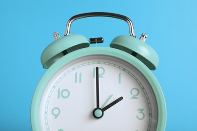 Turquoise alarm clock on light blue background, closeup