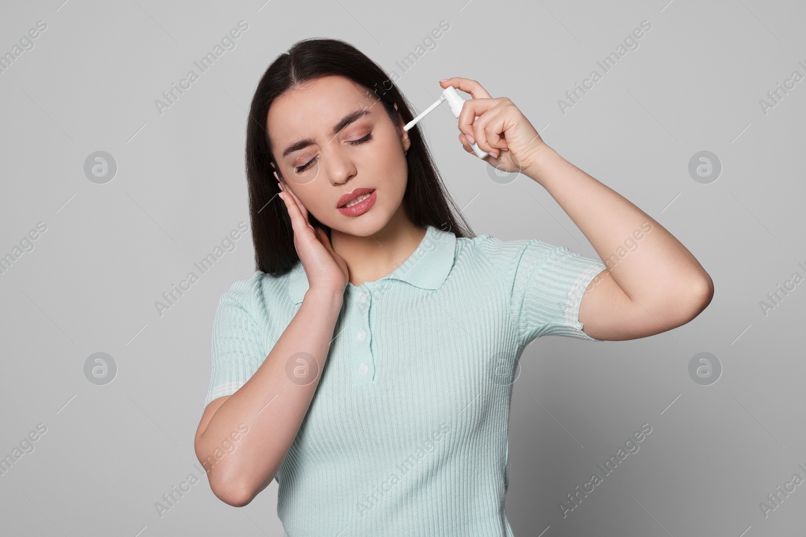 Photo of Young woman using ear spray on light grey background