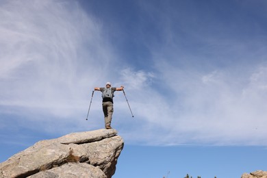 Man with backpack and trekking poles on rocky peak in mountains, back view