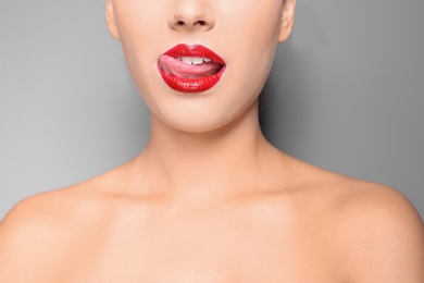 Photo of Beautiful young woman with red glossy lips on gray background, closeup