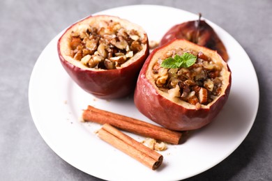 Tasty baked apples with nuts, honey, cinnamon sticks and mint on gray table, closeup