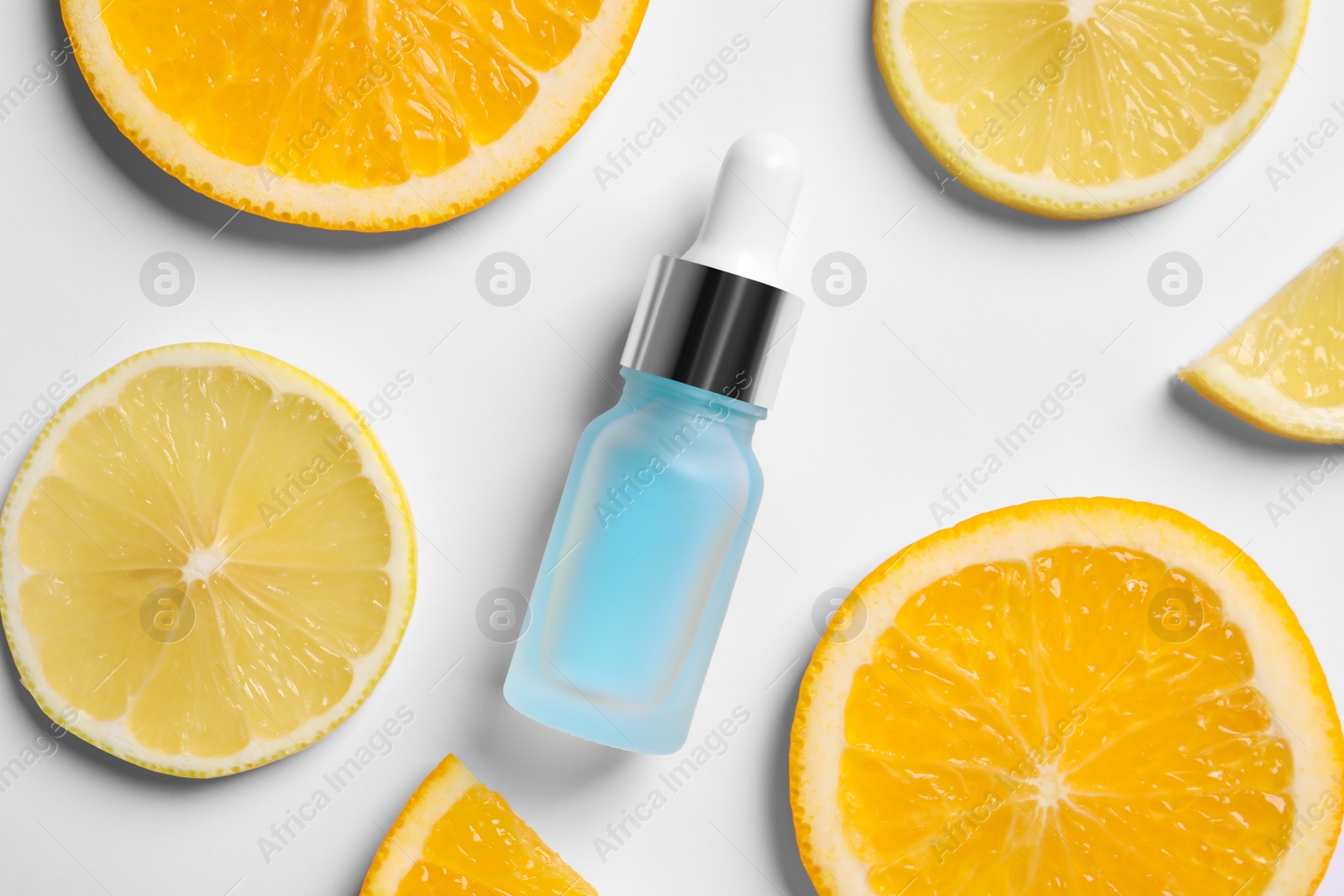 Photo of Bottle of cosmetic serum and sliced citrus fruits on white background, flat lay