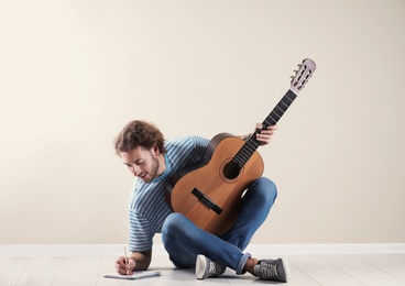 Young man with acoustic guitar composing song near grey wall